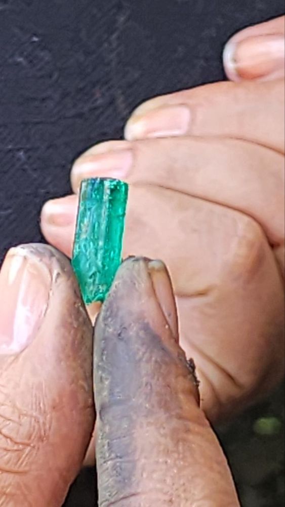 Cristal de esmeralda en bruto sostenido entre los dedos